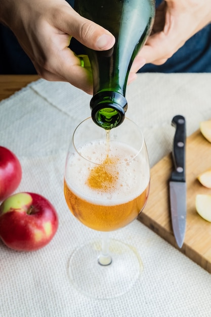 Zakończenie Wizerunek Mężczyzna Dolewania Premii Cidre W Szkle. Widok Z Góry Męskich Rąk, Wlewając Rocznika Wina Jabłkowego Do Pięknego Szkła W Rustykalnym Stole