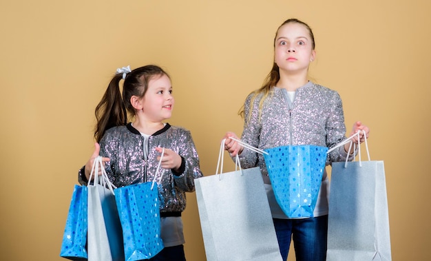 Zakupy i zakupy Czarny piątek Wyprzedaż i rabat Dzień zakupów Dzieci trzymają kilka paczek Moda dziecięca Oczekuj więcej Płać mniej Dziewczyny siostry przyjaciółki z torbami na zakupy beżowe tło