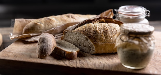 Zakwas żytni dojrzewający w słoiku wraz ze świeżym pieczywem na desce do krojenia