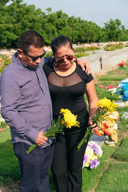 Żałoba starsza para trzymająca kwiaty w rękach i stojąca przy grobie na cmentarzu.