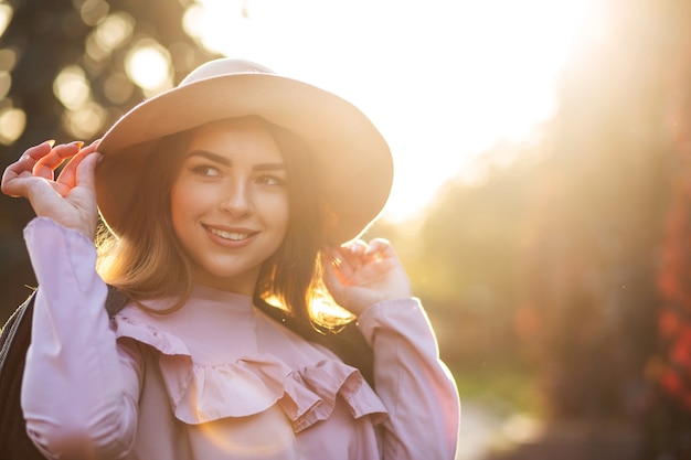 Zalotna uśmiechnięta kobieta z naturalnym makijażem w kapeluszu, ciesząca się ciepłą jesienną pogodą. Miejsce na tekst