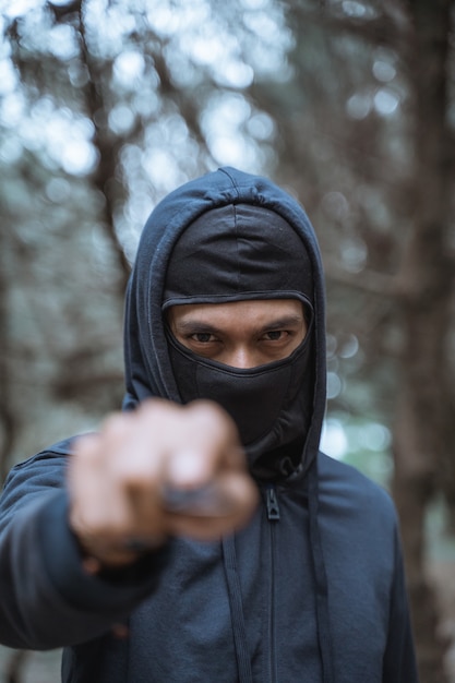 Zdjęcie zamaskowany mężczyzna z nożem w czarnym ubraniu z groźnymi oczami lasu