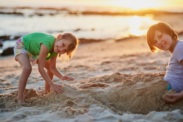 Zamierzamy zbudować największy zamek z piasku w historii Portret dwójki młodego rodzeństwa bawiącego się razem w piasku na plaży?