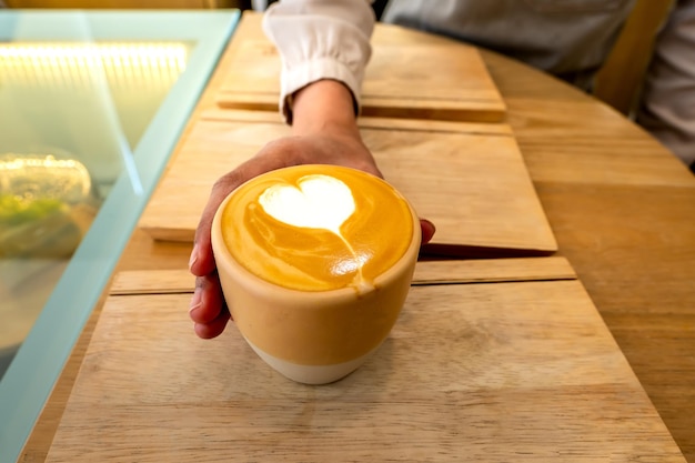 Zamknij filiżankę kawy z Cappuccino lub powierzchnią pianki mlecznej latte art, trzymając w dłoni dziewczyny