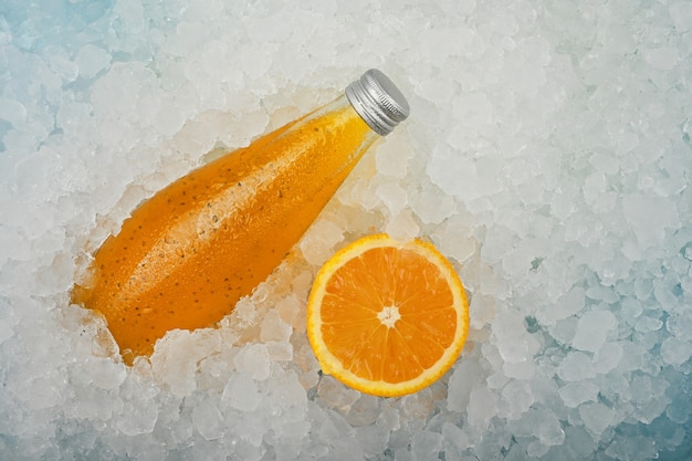 Zamknij jedną szklaną butelkę zimnego napoju koktajlowego z soku pomarańczowego z nasionami chia i połową pomarańczy na kruszonym lodzie na wystawie detalicznej, podwyższony widok pod dużym kątem, bezpośrednio nad