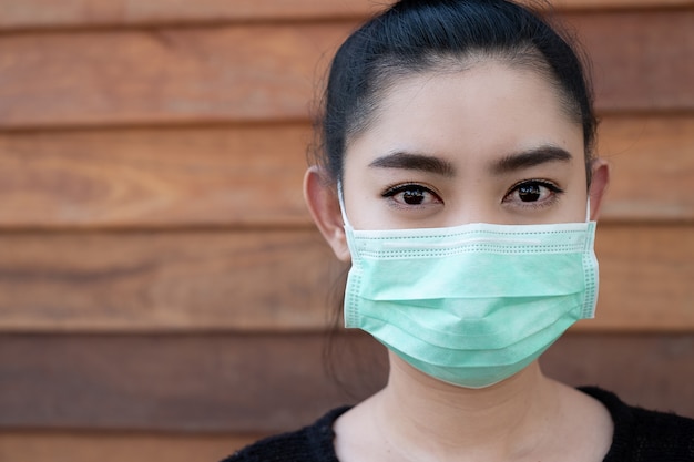 Zamknij Się Młoda Kobieta Asia Nakładająca Maskę Medyczną W Celu Ochrony Przed Unoszącymi Się W Powietrzu Chorobami Układu Oddechowego, Jak Grypa Covid-19 Pm2.5 Kurz I Smog Na ścianie Drewnianej ścianie