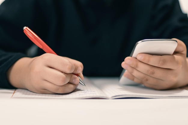 Zamknij się młody student z smartphone pisania do notebooka.