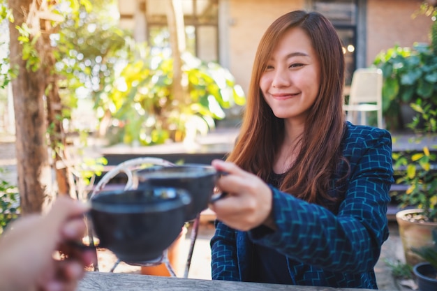Zamknij się obraz pięknej azjatyckiej kobiety, stukając kubki do kawy z przyjacielem w kawiarni