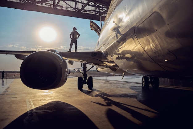 Zdjęcie zamknij się obraz silnika dużego samolotu pasażerskiego w hangarze lotniczym, podczas gdy pilot stoi na skrzydle