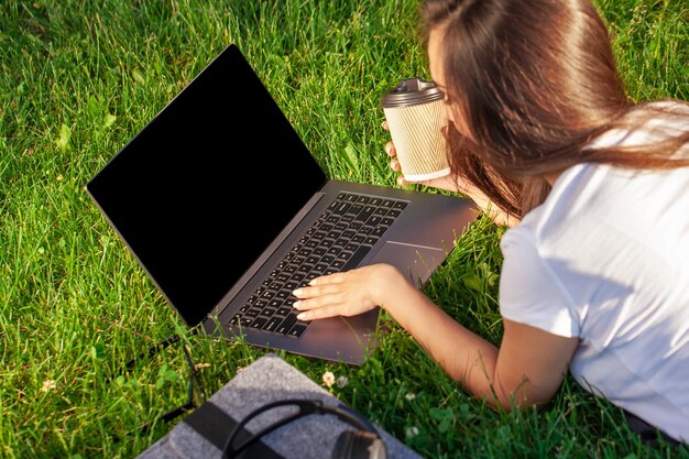 Zamknij się ręce na klawiaturze. Kobieta pracująca na komputerze przenośnym z pustym czarnym pustym ekranem, aby skopiować miejsce w parku na zielonej trawie słoneczny trawnik na zewnątrz.