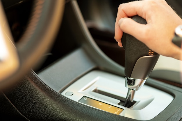 Zamknij się z kobieta kierowca trzymając rękę na automatycznej dźwigni zmiany biegów jazdy jako samochód.