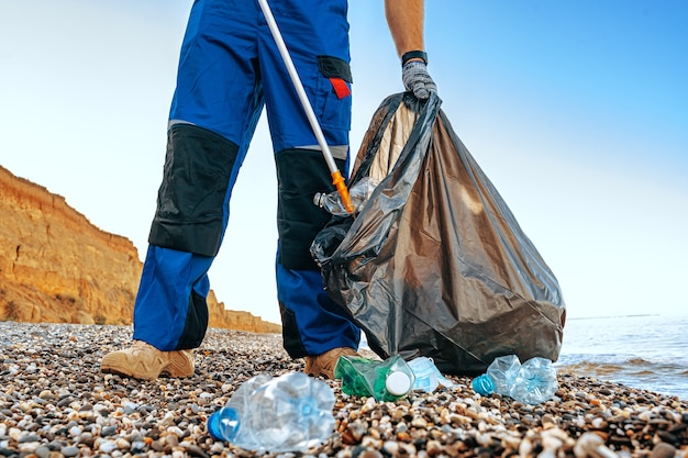 Zamknij się zdjęcie mężczyzny zbierającego śmieci za pomocą narzędzia chwytającego na plaży w pobliżu oceanu