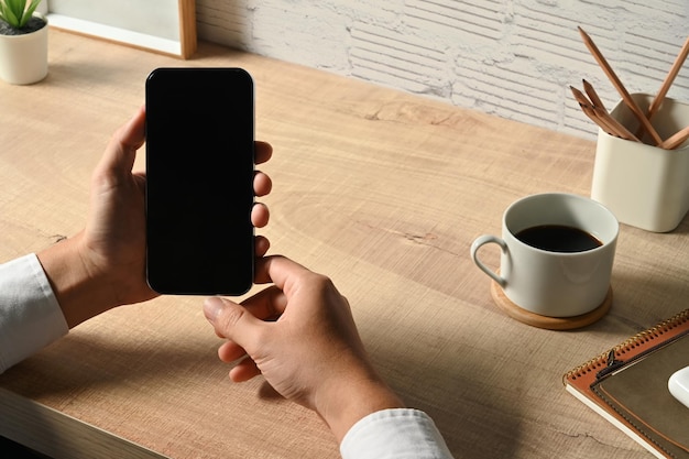Zamknij widok biznesowych rąk trzymających inteligentny telefon na drewnianym biurku Pusty ekran dla Twojego projektu reklamowania