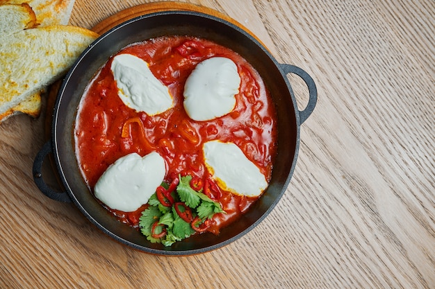 Zamknij widok na shakshuka z ostrą papryczką chili w soku pomidorowym z dodatkiem ciecierzycy, sera i papryki. Tradycyjna kuchnia izraelska