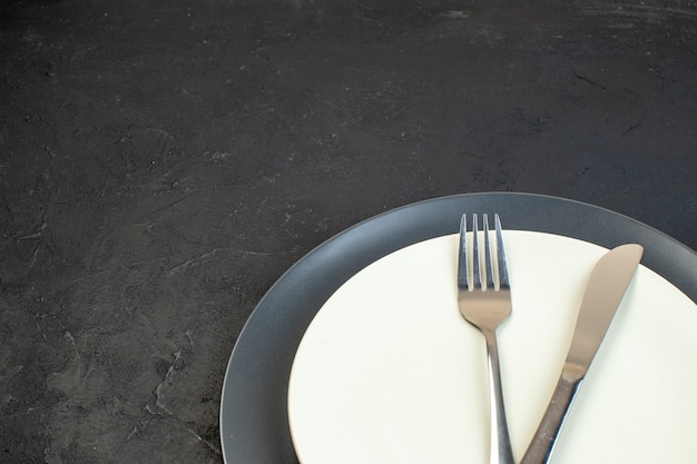 Zamknij widok sztućców ustawionych na ciemnym kolorze i białych pustych talerzy w różnych rozmiarach na czarnym tle