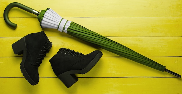 Zamszowe czarne buty, parasol na żółtym tle drewna. Widok z góry