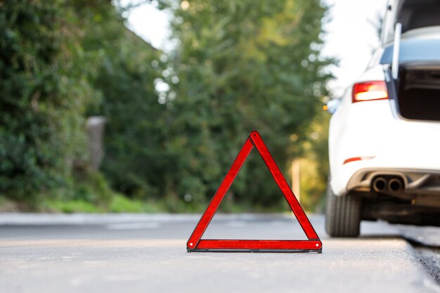 Zamyka up czerwony ostrzegawczy trójboka znaka symbol i łamany biały samochód na poboczu