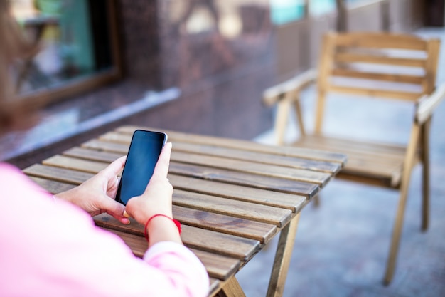 Zamyka up smartphone w młodych żeńskich rękach w ulicznej kawiarni.