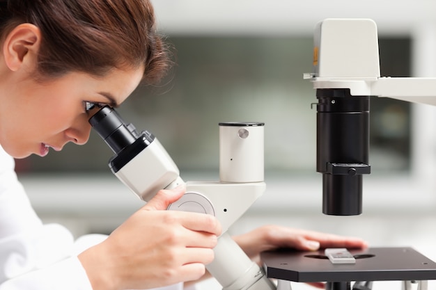 Zamyka up żeński nauka uczeń patrzeje w mikroskopie