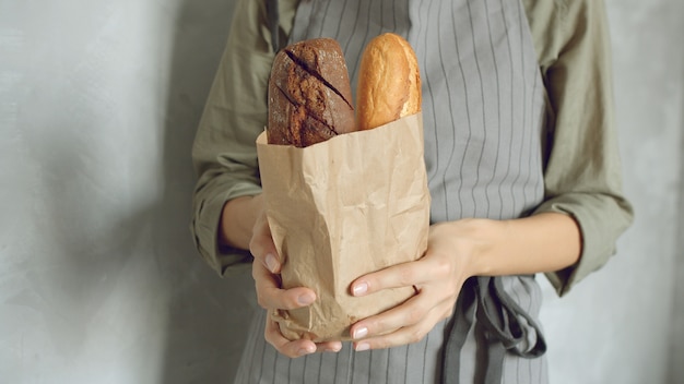 Zamyka up żeńskie ręki piekarz lub sprzedawca w jednolitego mienia smakowitych baguettes na szarym tle