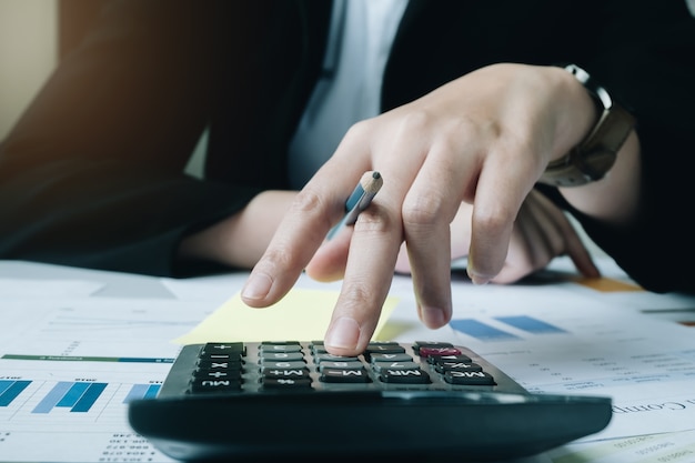 Zamyka w górę Biznesowej kobiety używa kalkulatora dla robi matematyki finansowi na drewnianym biurku w biurze
