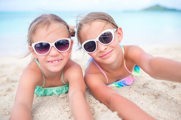 Zamyka W Górę Małych Dziewczynek Na Piaskowatej Plaży. Szczęśliwe Dzieci Leżące Na Białej, Ciepłej, Piaszczystej Plaży