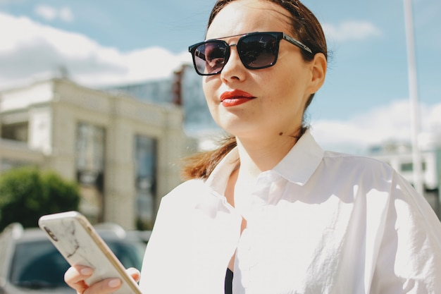 Zamyka w górę portreta brunetki eleganckiej kobiety biznesowa dama w okularach przeciwsłonecznych używać wiszącą ozdobę