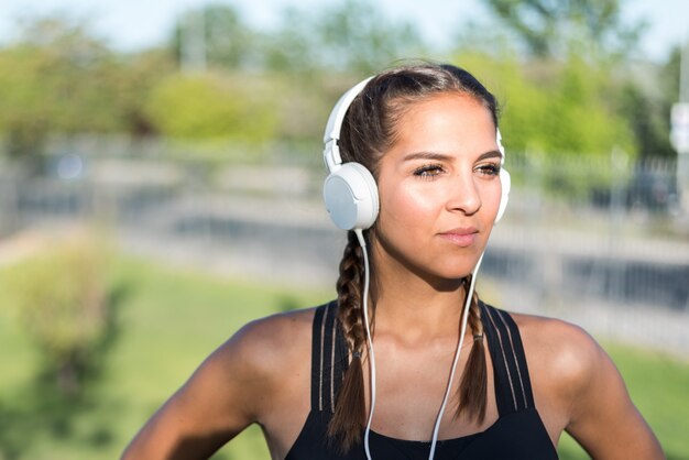 Zamyka w górę portreta kobieta robi sportowi odpoczywać plenerową uśmiechniętą i słuchającą muzykę