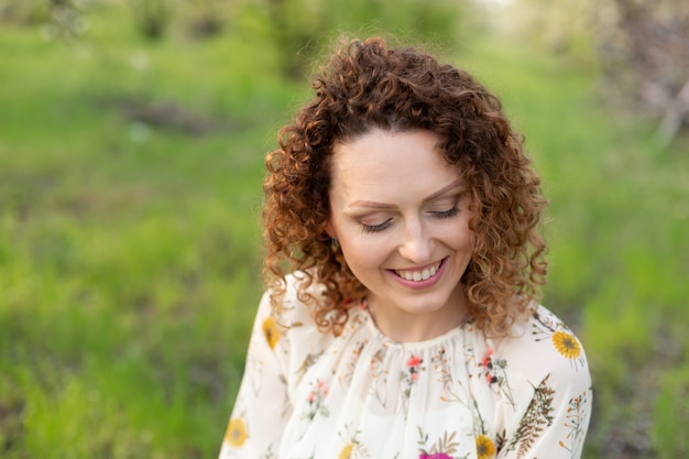 Zamyka w górę portreta młoda uśmiechnięta atrakcyjna kobieta z kędzierzawym włosy w zielonym kwiatonośnym wiosna parku. Czyste emocje
