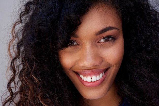 Zamyka w górę uśmiechniętej młodej amerykanin afrykańskiego pochodzenia kobiety przeciw szarości ścianie