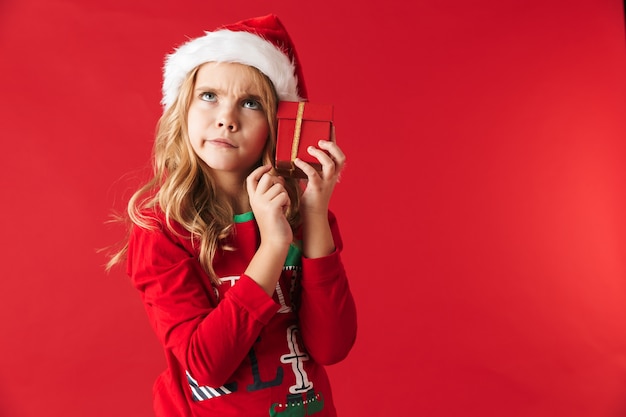 Zamyślona dziewczynka ubrana w świąteczny kostium stojący na białym tle, trzymając pudełka na prezenty