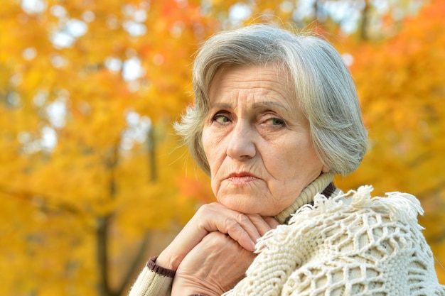 Zamyślona starsza kobieta na tle jesiennych liści