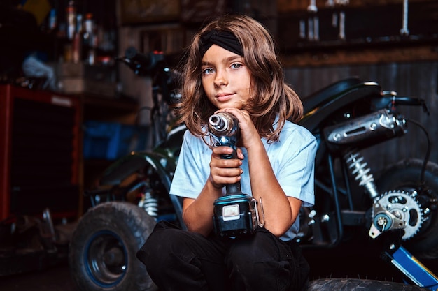 Zamyślony beautivul dzieciak pozuje ze śrubokrętem w warsztacie samochodowym.