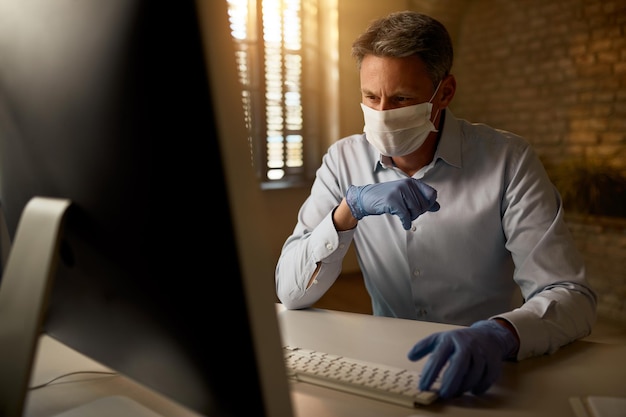 Zamyślony Biznesmen Noszący Maskę Podczas Pracy Na Komputerze Stacjonarnym W Biurze Podczas Epidemii Wirusa