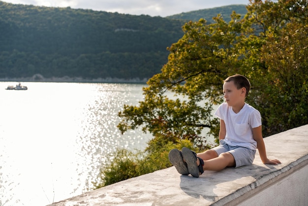 zamyślony chłopiec podziwiający widok na jezioro, podróżujący i aktywny tryb życia