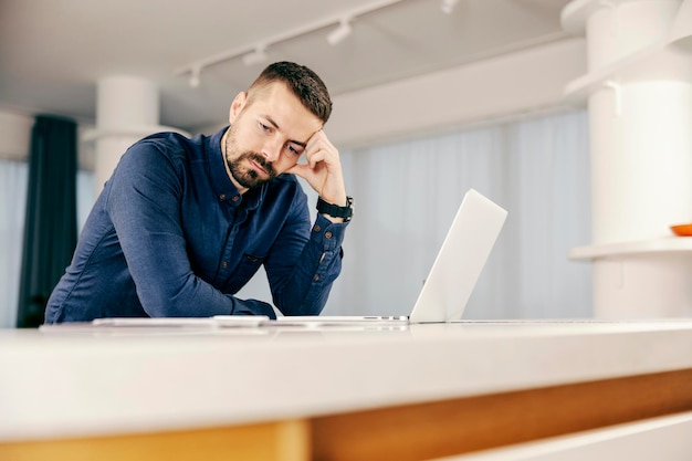 Zamyślony mężczyzna używający laptopa w domu i myślący o rozwiązaniu