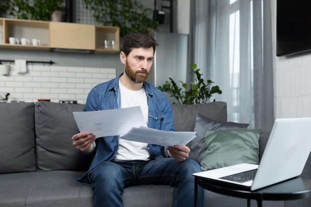 Zamyślony mężczyzna w domu pracujący na laptopie freelancer na papierze skupiony i poważny