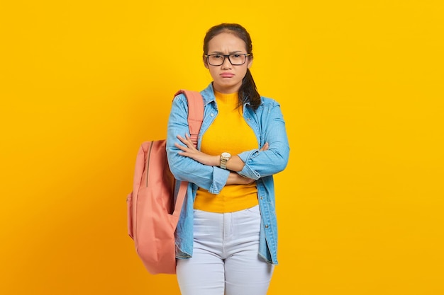 Zamyślony młody azjatycki student w dżinsowym stroju z plecakiem skrzyżowanym w klatce piersiowej i wyglądającym pewnie na żółtym tle Edukacja w koncepcji college'u w liceum