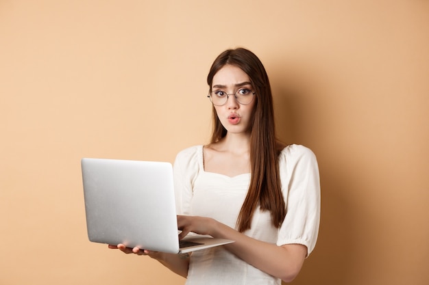 Zaniepokojona dziewczyna w okularach patrzy na kamerę zdezorientowana pracując na laptopie, mająca problem ze sta...