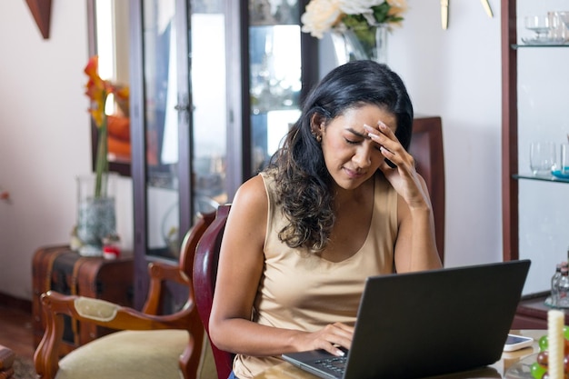 Zaniepokojona latynoska z czarnymi włosami pracuje nad laptopem w salonie.