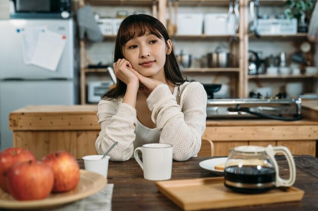 Zapamiętaj dawną dobrą zabawę z przyjaciółmi, przerwę na kawę z jabłkami. Długie włosy młoda Azjatycka kobieta siedzi elegancji przed kuchnią drewnianą.