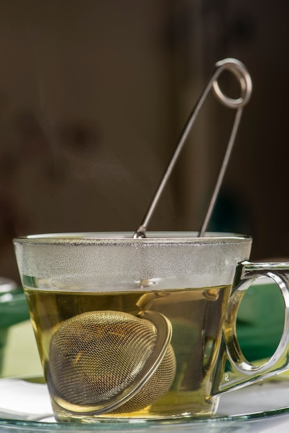 Zaparzacz z herbatą w filiżance z gorącą wodą.