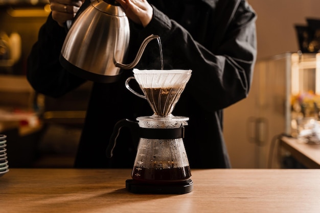 Zaparzanie kawy przelewowej Barista nalewa gorącą wodę na filtr z kawą mieloną w lejku Zalewanie alternatywną metodą nalewania wody na zmielone ziarna kawy znajdujące się w filtrze