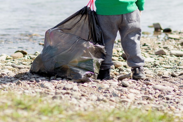 Zapisz koncepcję środowiska małego chłopca zbierającego śmieci i plastikowe butelki na plaży, aby wyrzucić je do kosza