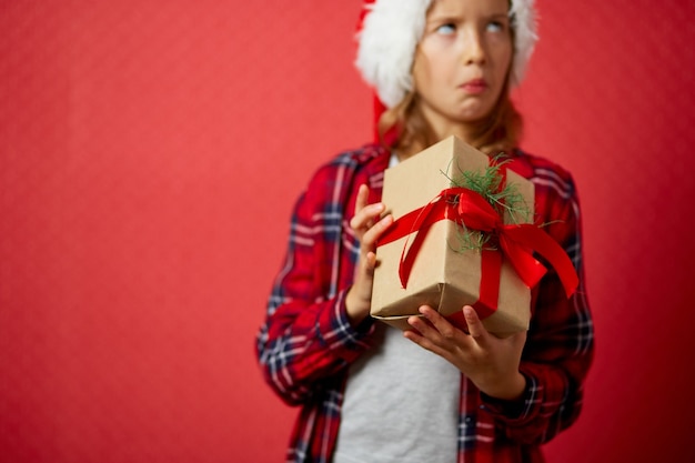 Zaskoczona i pozytywna dziewczynka w santa hat trzymająca świąteczny prezent