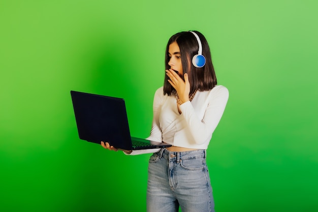 Zaskoczona kobieta w słuchawkach trzymająca laptop, podnosząca z podniecenia rękę, otrzymała w sieci szokujące wieści.