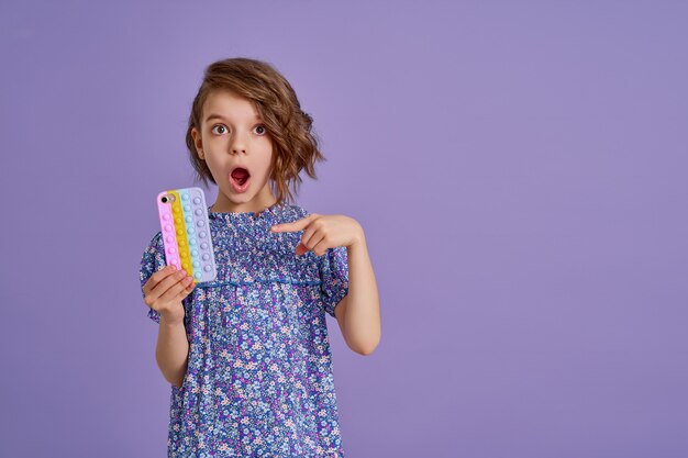 Zaskoczona mała dziewczynka trzymająca telefon z otwartymi ustami na fioletowym tle