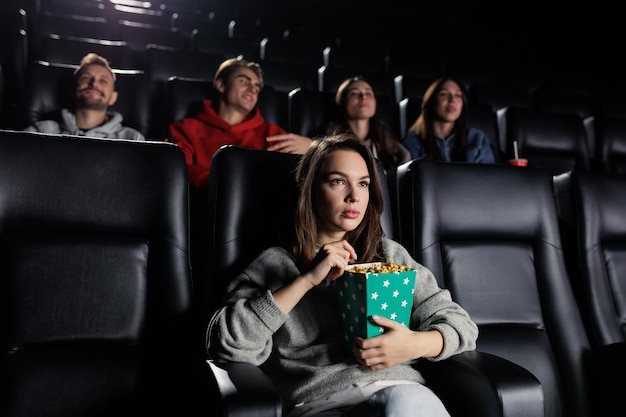 Zaskoczona młoda kobieta je popcorn na premierze filmu w kinie Weekendowy wieczorny wypoczynek