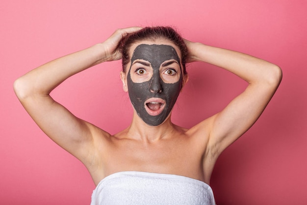 Zaskoczona młoda kobieta z maską na twarzy wiąże włosy w domowej pielęgnacji