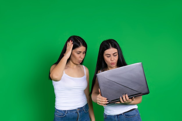 Zaskoczone bliźniaczki w zwykłych ubraniach patrzą na laptopa
